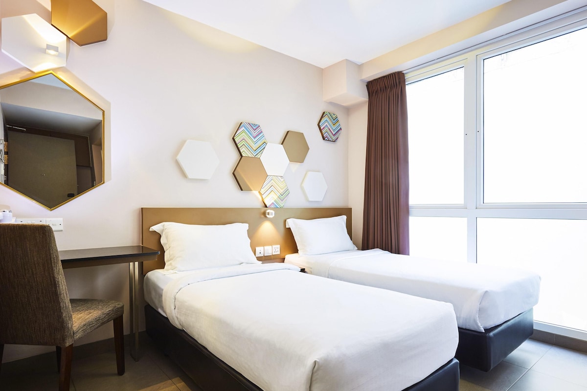 A hotel room with two beds, a desk, a chair, a large mirror, and decorative wall art.