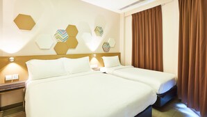 A hotel room with two beds, a wall-mounted light fixture, and a window with brown curtains. - ibis budget Singapore Imperial (Singapore)