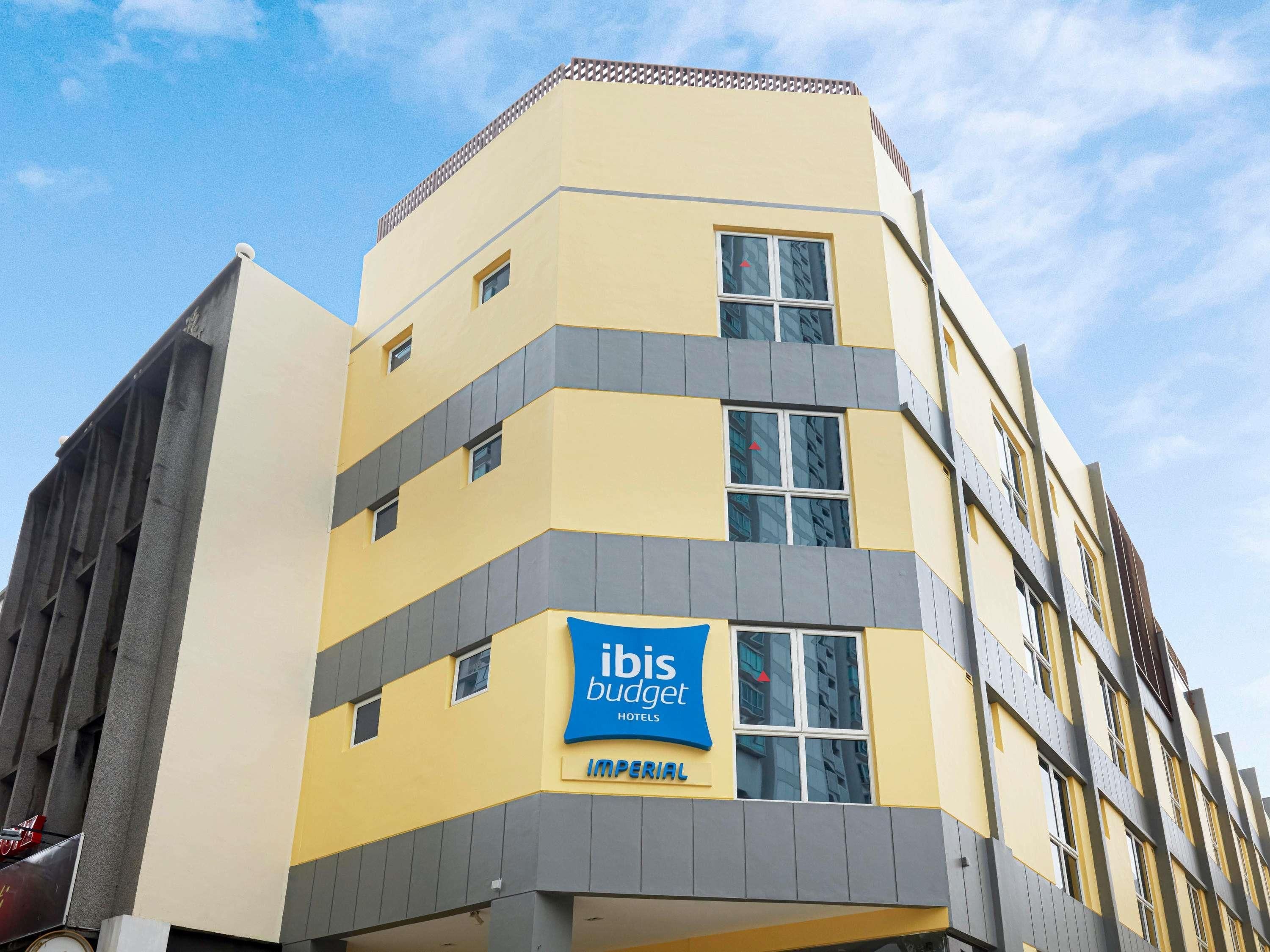 Um hotel de vários andares com fachada amarela, um letreiro azul para hotéis ibis budget e uma entrada visível.