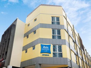 Un hotel de varios pisos con fachada amarilla, un letrero azul para ibis budget hotels y una entrada visible.