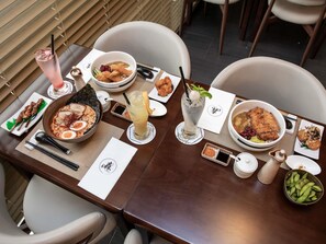 Una mesa de comedor con diversos platos, una bebida, palillos y un menú.