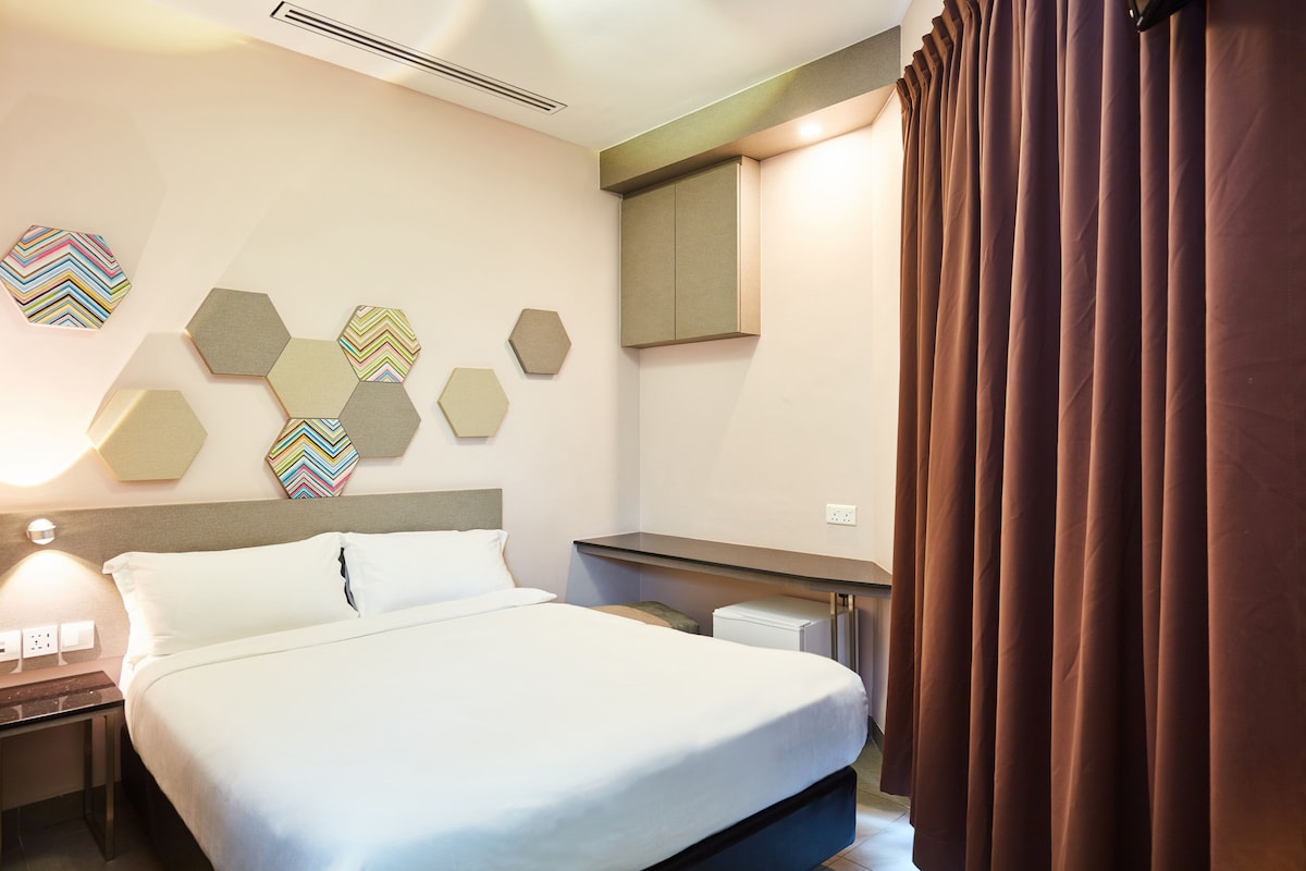 Una habitación de hotel con cama, mesitas de noche, un escritorio y una pared decorada con hexágonos.