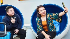 Two people seated in blue, curved chairs in a room with a white wall and a colorful painting. - ibis budget Singapore Imperial (Singapore)