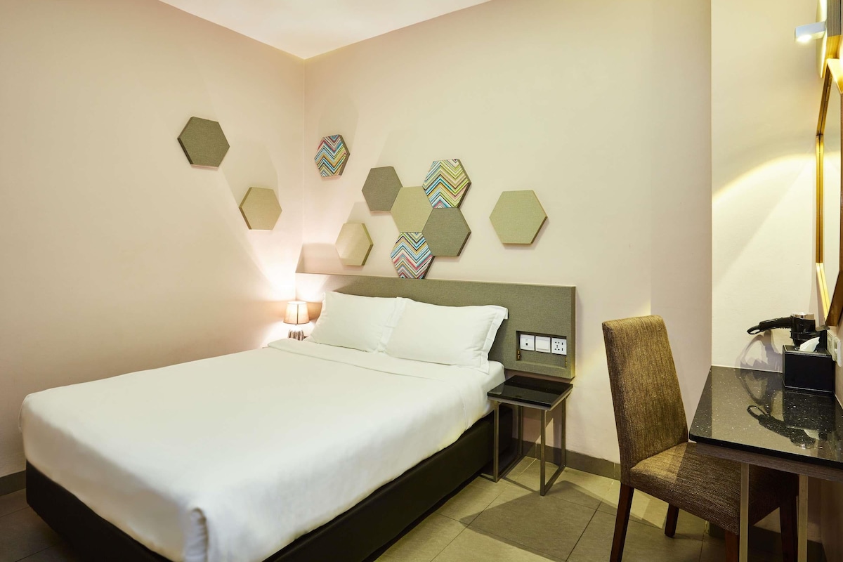 A hotel room with a bed, a nightstand, a chair, a desk, and hexagonal wall decorations.