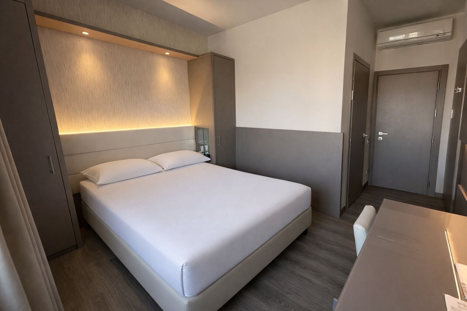 Una camera d'albergo moderna con un letto grande, un comodino, un armadio e un condizionatore d'aria integrato.