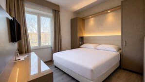Habitación de hotel con cama, escritorio, televisor y ventana con cortinas.