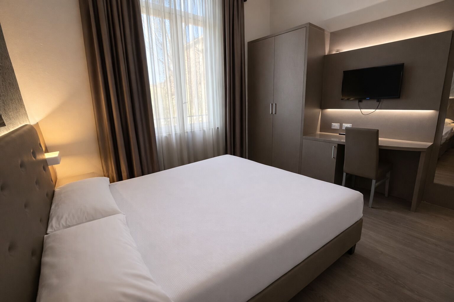 Una habitación de hotel con cama, escritorio, silla, televisor y armario.