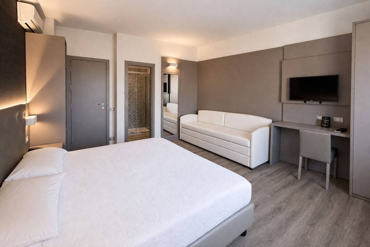 Una habitación de hotel moderna con una cama grande, un sofá, un escritorio y un televisor de pantalla plana, además de un vestidor.