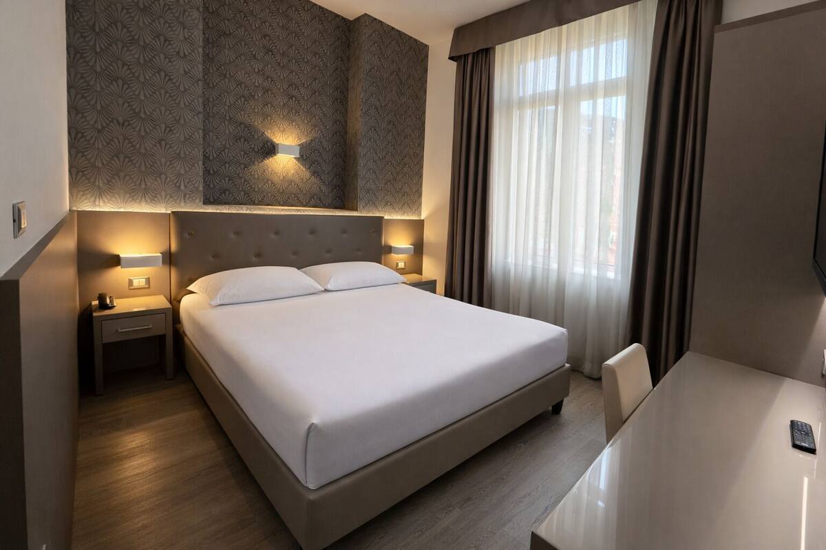 Una habitación de hotel con una cama grande, mesitas de noche, un escritorio y un televisor.