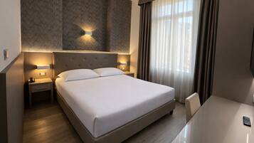 A hotel room with a large bed, bedside tables, a desk, and a TV.