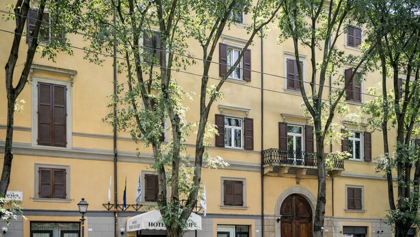 Un edificio amarillo con múltiples ventanas, una entrada central con una puerta de madera grande y un balcón en el piso superior.