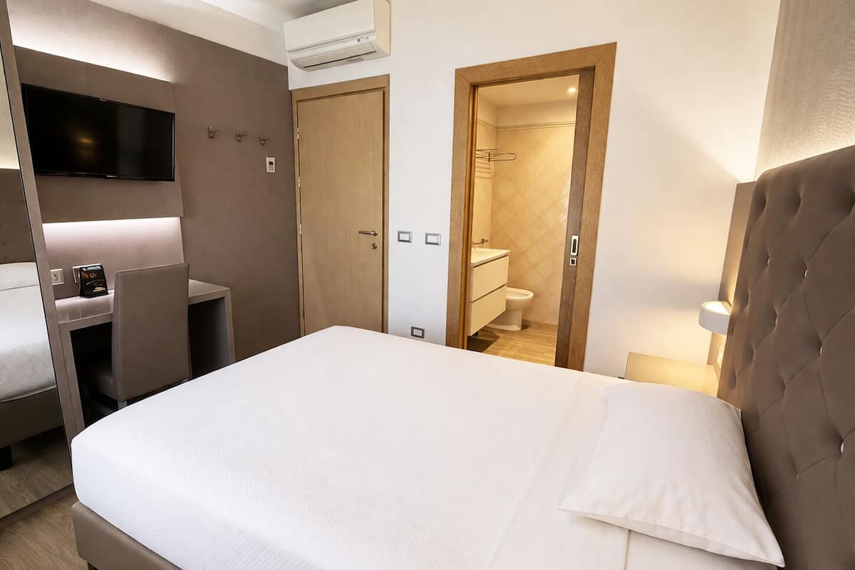 Habitación de hotel con cama, escritorio, televisor, aire acondicionado, baño y puerta.