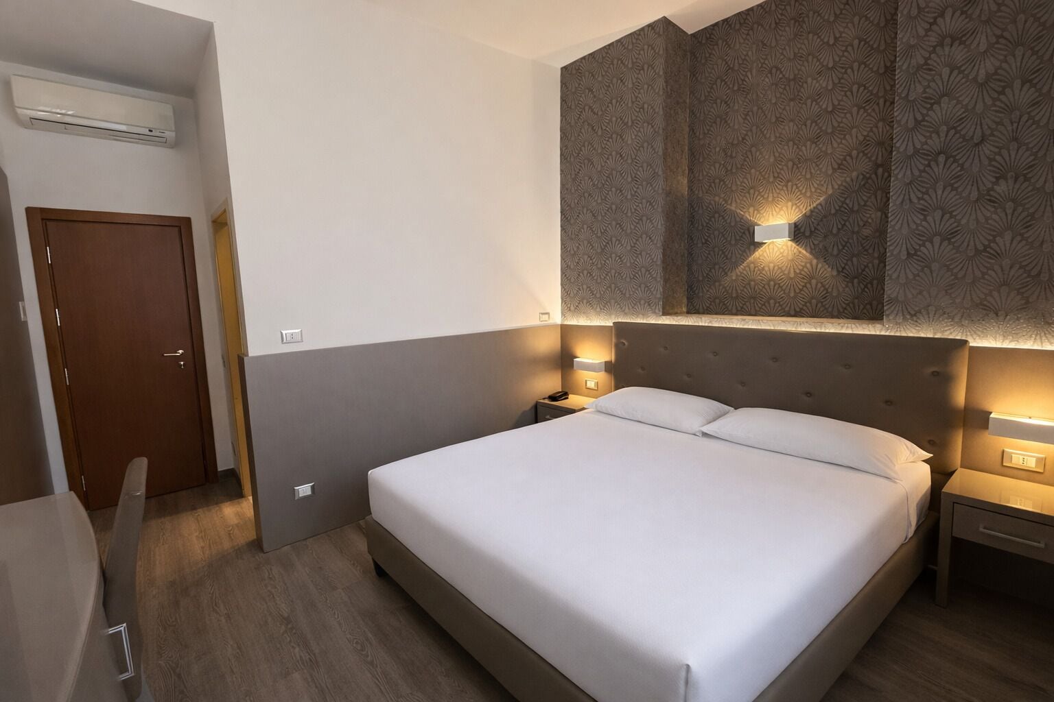 Une chambre d’hôtel équipée d’un lit, de tables de chevet, d’une armoire et d’un appareil de climatisation.