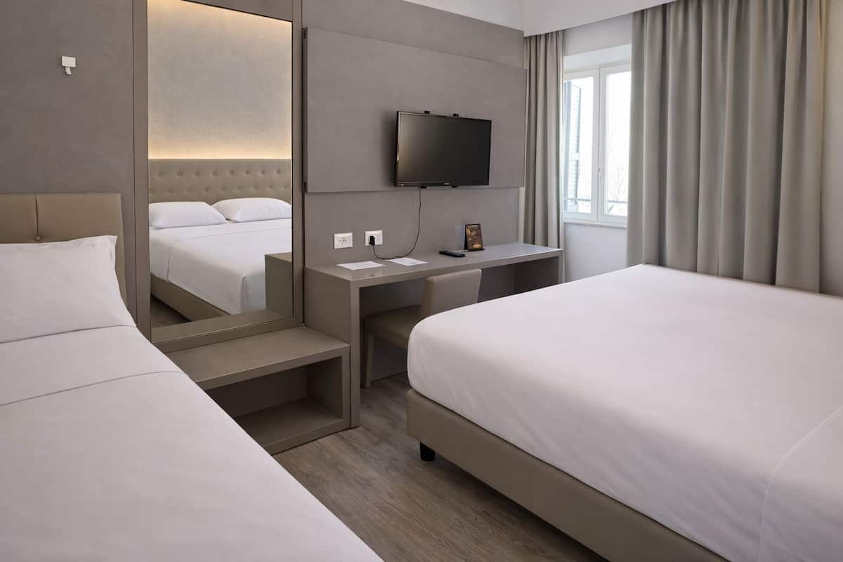 Habitación de hotel con dos camas, un escritorio, televisión de pantalla plana, espejo y ventana con cortinas.