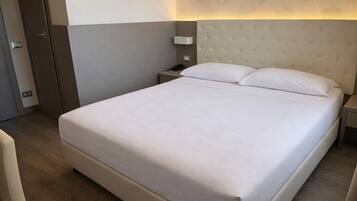 A hotel room with a large bed, a nightstand, a bedside table, and a wall-mounted lamp.