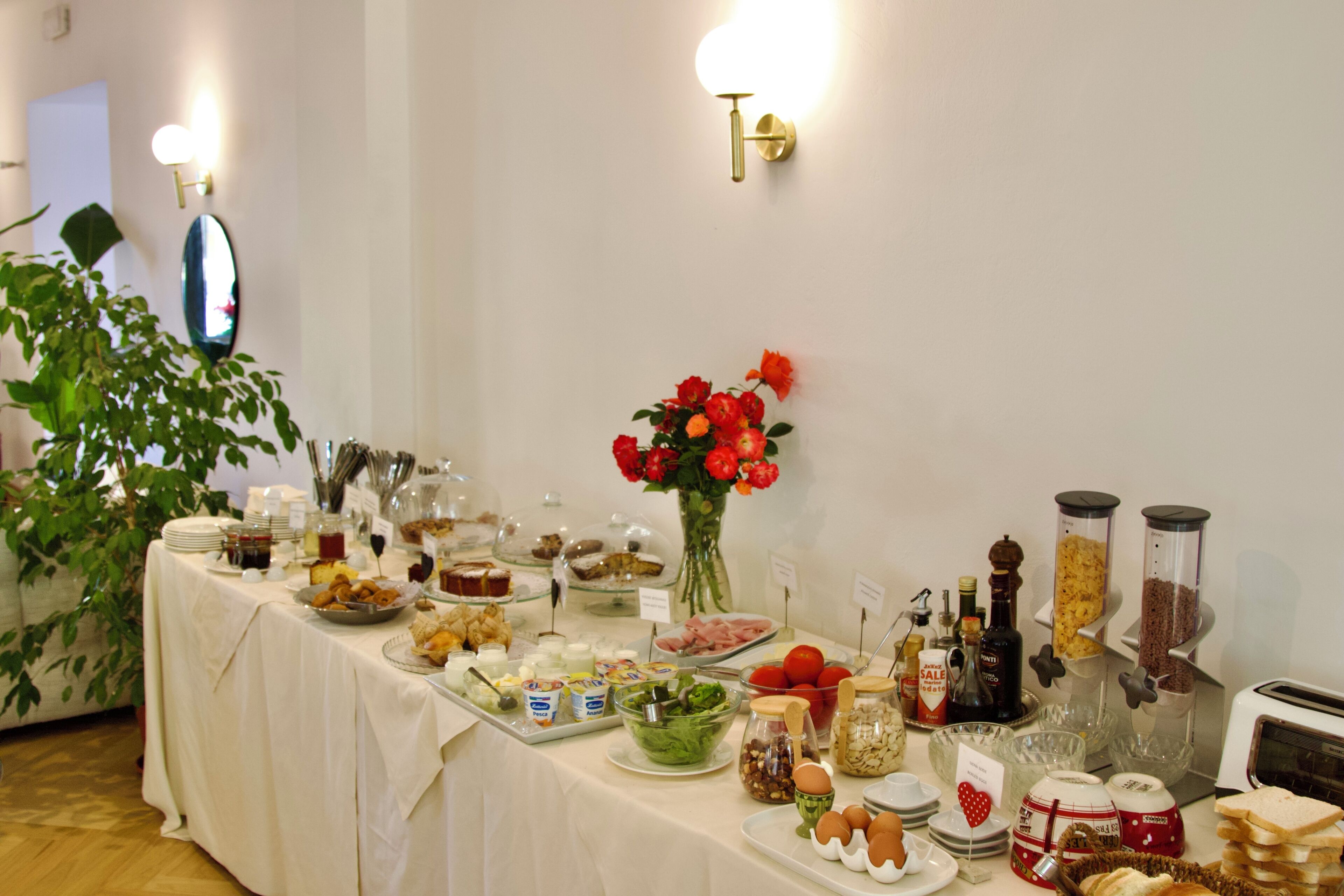 A buffet table with various food items, a vase of red flowers, and a toaster.