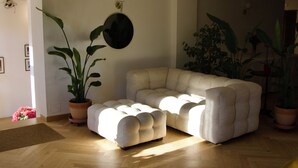 A living room with a sectional sofa, potted plants, and a round mirror on the wall.