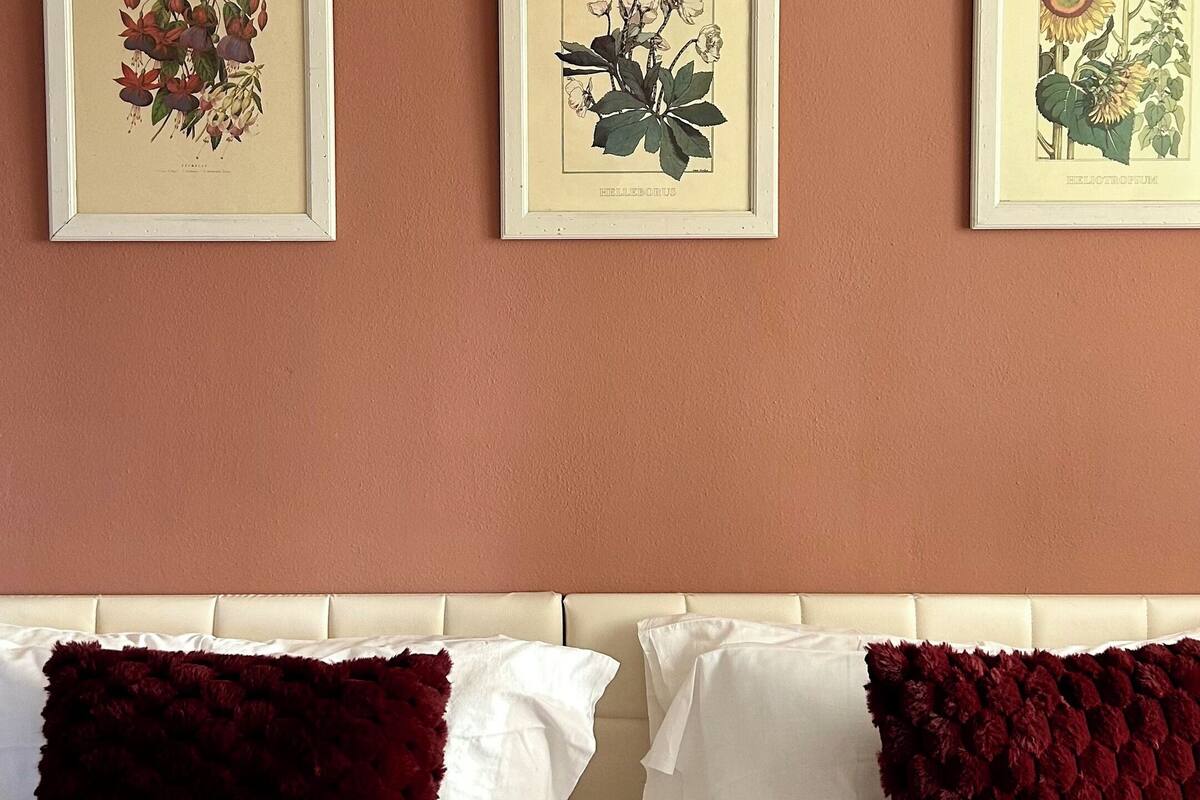 A bedroom with a bed, two pillows, and three framed botanical prints on the wall.