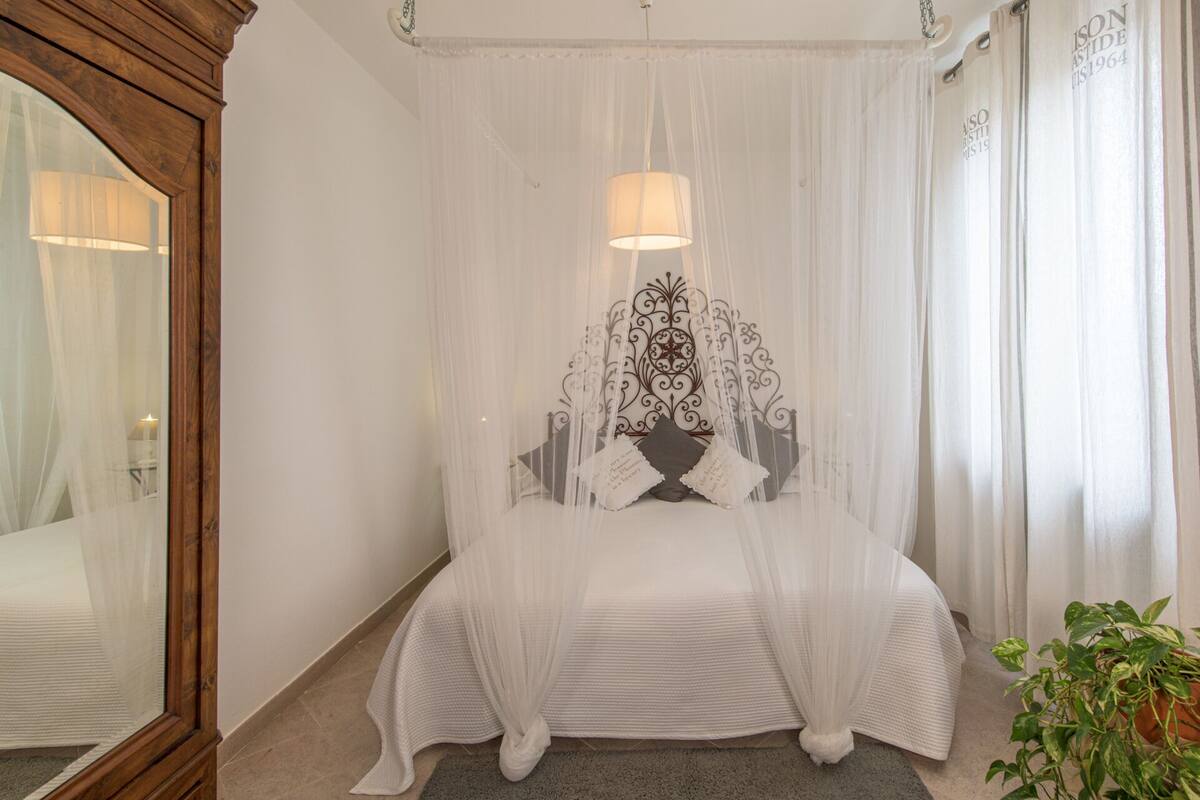 A bedroom with a canopy bed, a mirror, and a potted plant.
