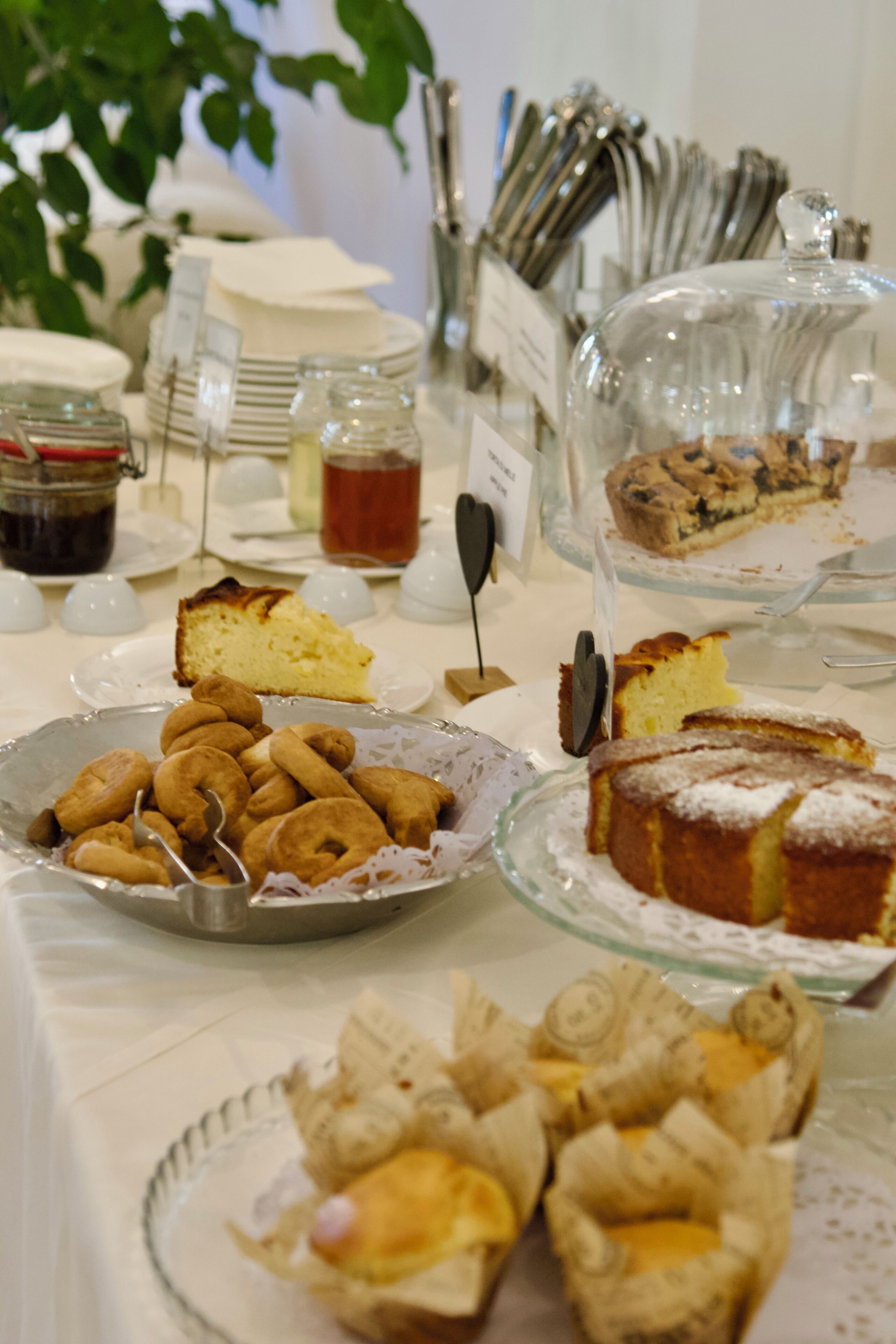 Un bufé con diversos postres y pastelería, incluyendo pasteles y galletas, sobre platos de vidrio y en una vitrina de cristal.