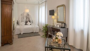 A hotel room with a bed, bedside table, mirror, and a glass table with snacks and drinks.