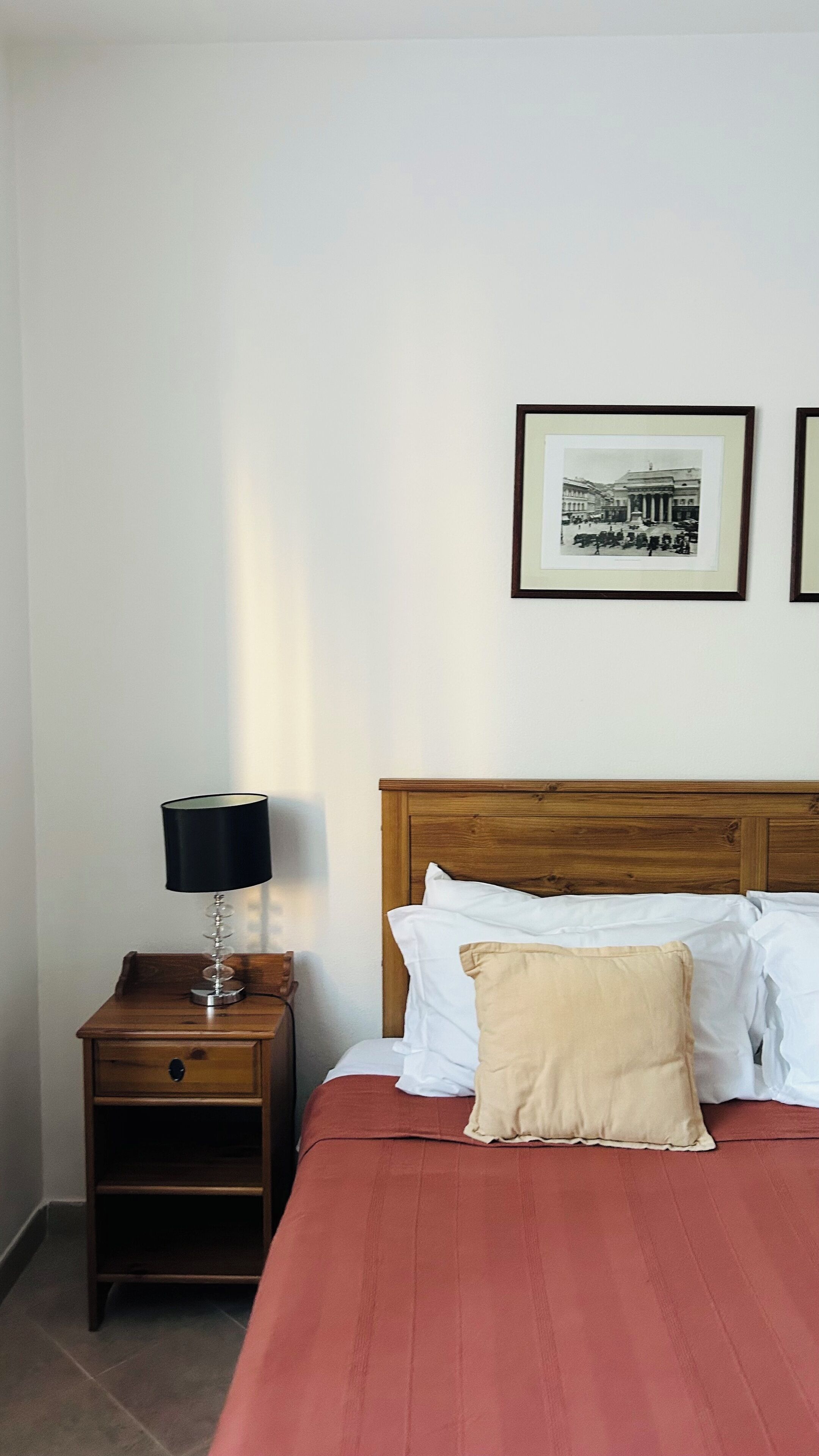 A neatly arranged bedroom with a wooden headboard, a bedside table with a lamp, and a bed with white and beige pillows.