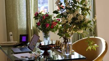 Ein Glastisch mit einem Laptop, einer Blumenvase, einem Stuhl und einem Fenster mit Vorhängen.