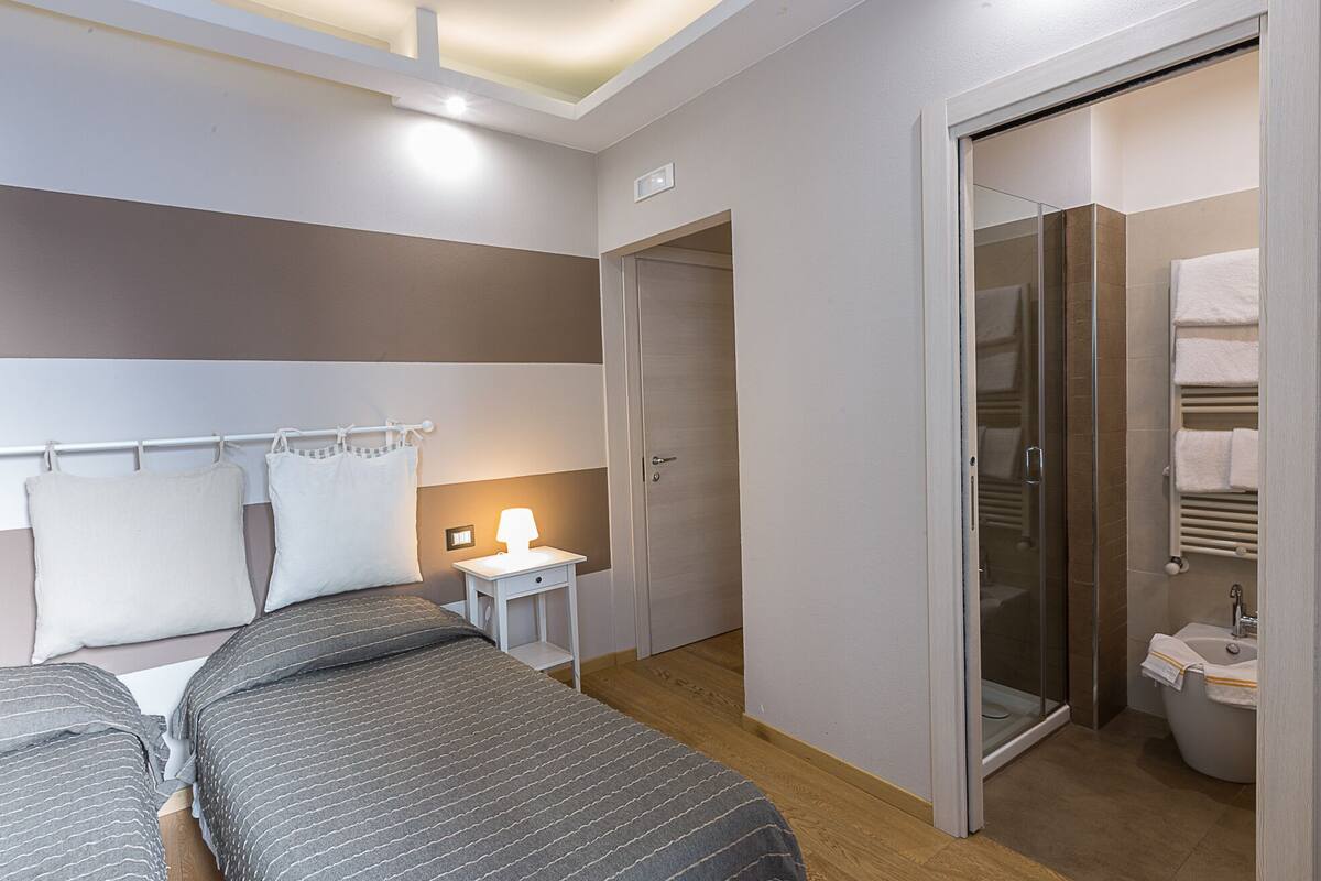A bedroom with a bed, bedside table, lamp, and a glass-enclosed shower area.