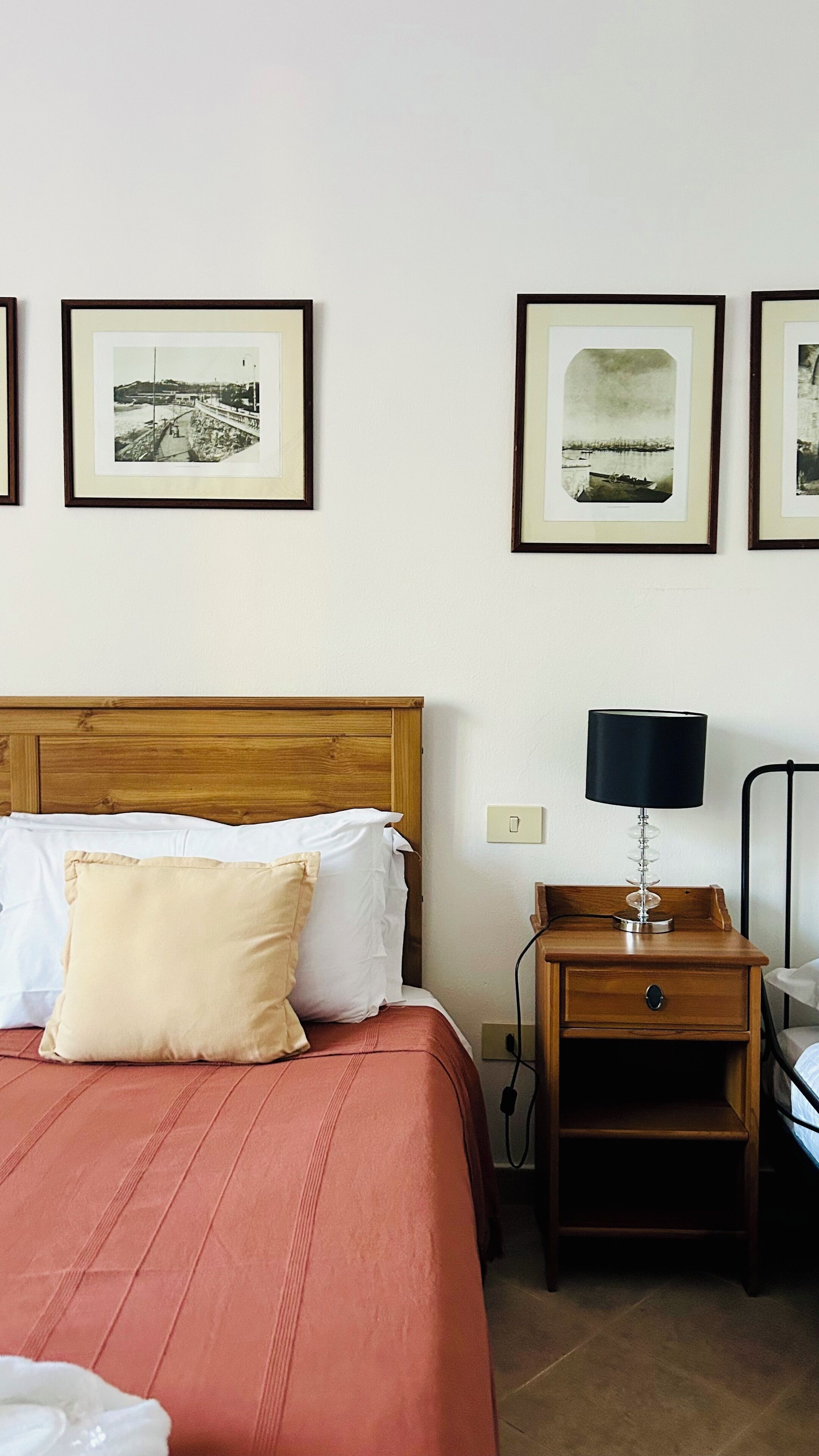 A hotel room with a wooden bed, a nightstand, a lamp, and framed pictures on the wall.