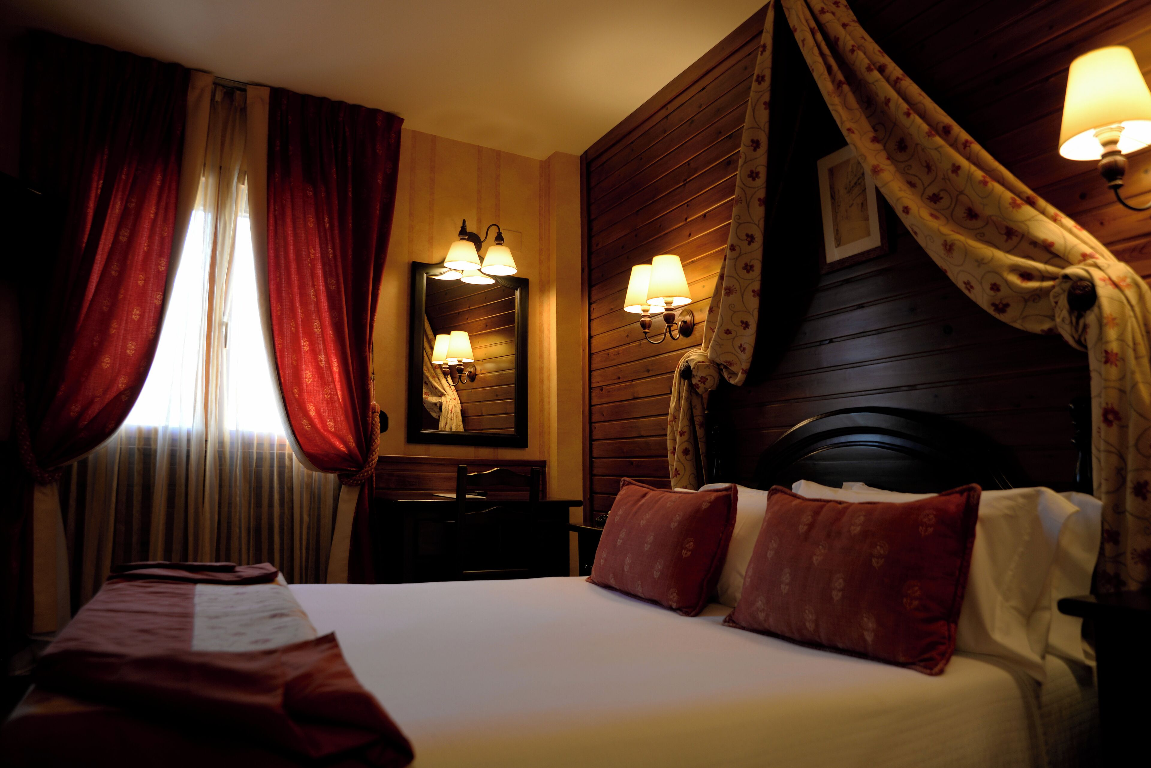A hotel room with a large bed, a desk, and two wall-mounted lamps.
