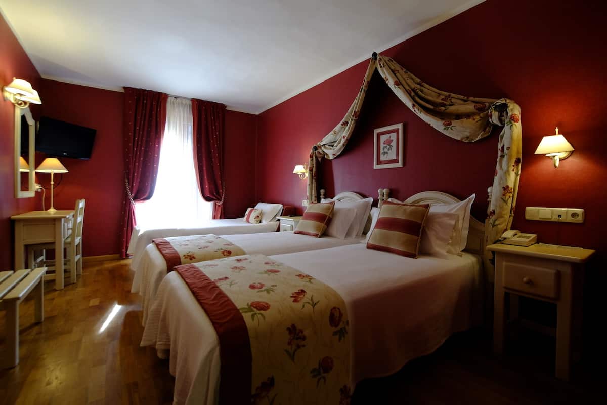 A hotel room with two beds, a desk, and a TV.