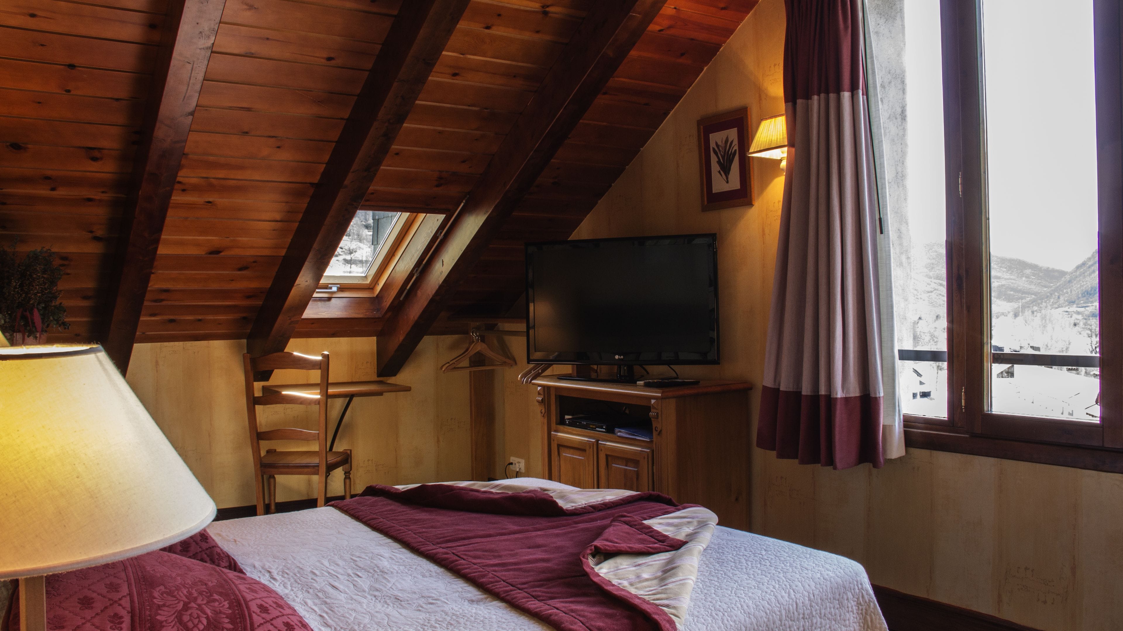 Una habitación acogedora con una cama, televisión, escritorio y ventana con vistas a las montañas.