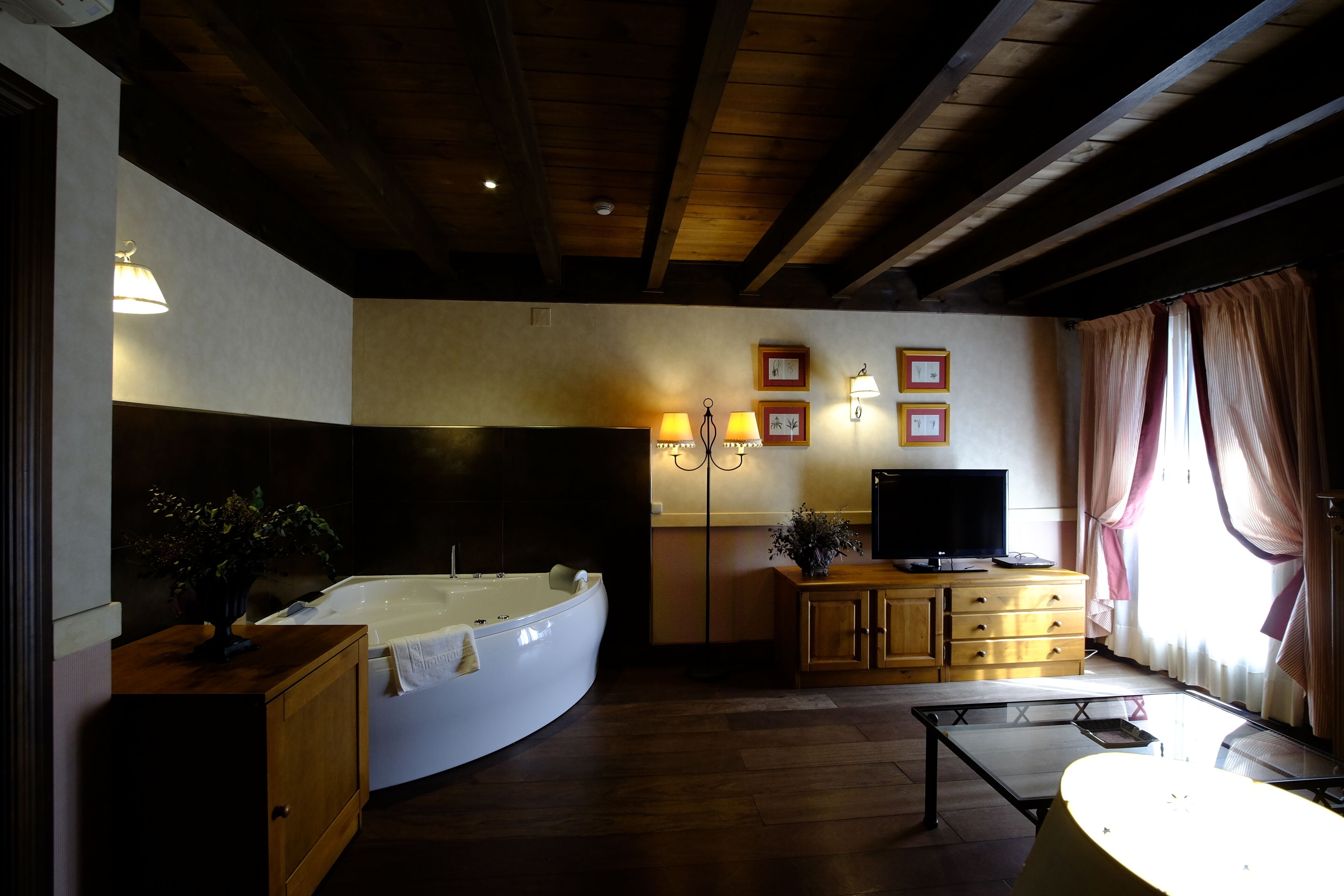 A room with a large bathtub, wooden cabinets, a television, and framed pictures on the wall.