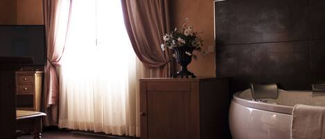 A hotel room with a wooden cabinet, a vase with flowers, a large bed, and a window with curtains.