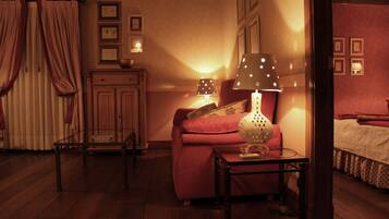 Una habitación acogedora con piso de madera, un sofá rojo, una mesita con una lámpara y una cama con cubrecama blanco.