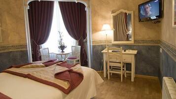 A hotel room with a bed, a desk, a chair, a television, and a window with curtains.