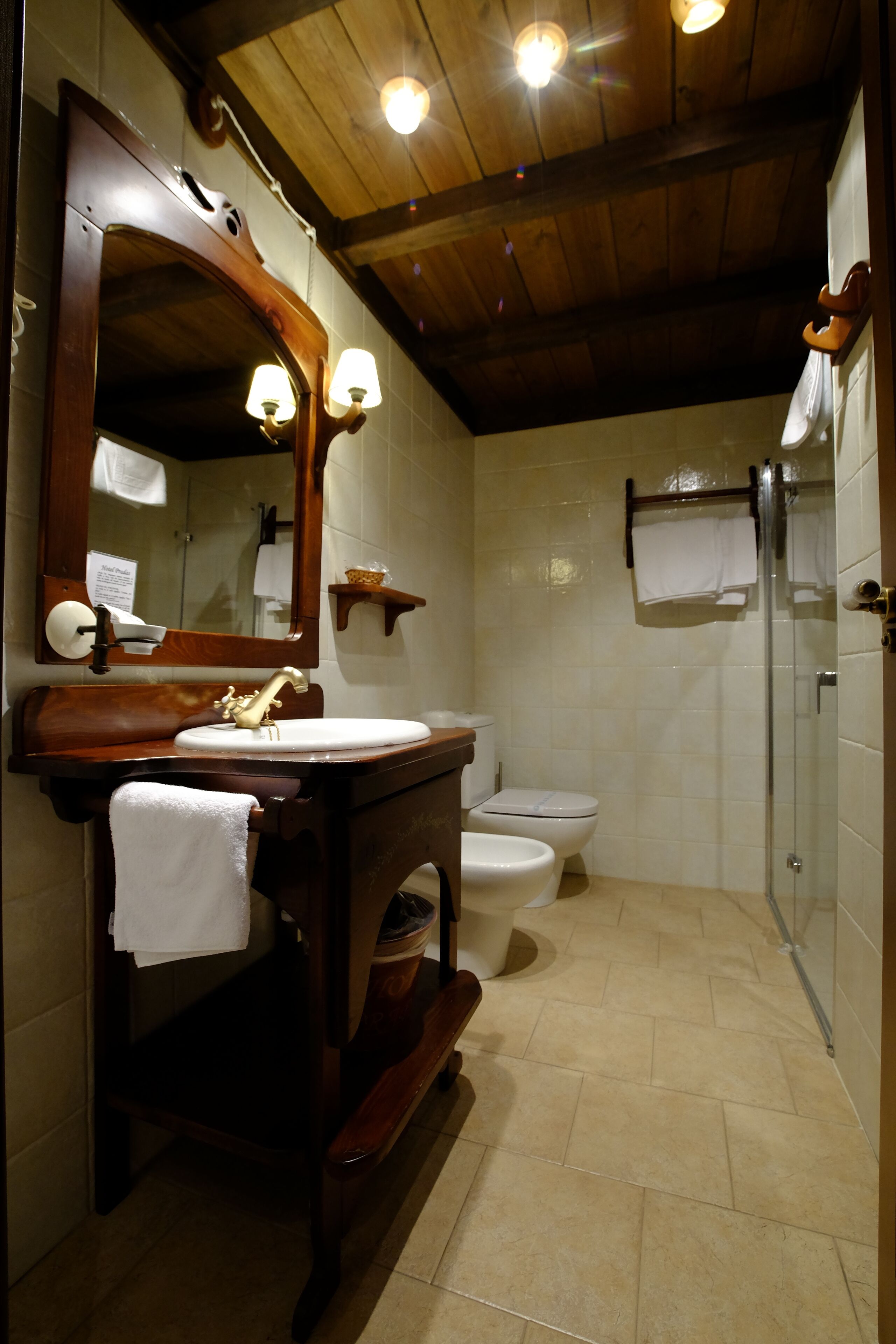 A bathroom with a wooden vanity, a large mirror, a toilet, and a glass shower enclosure.