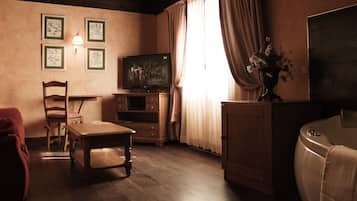 Una habitación acogedora con suelo de madera, televisión, escritorio, silla, armario y ventana con cortinas.