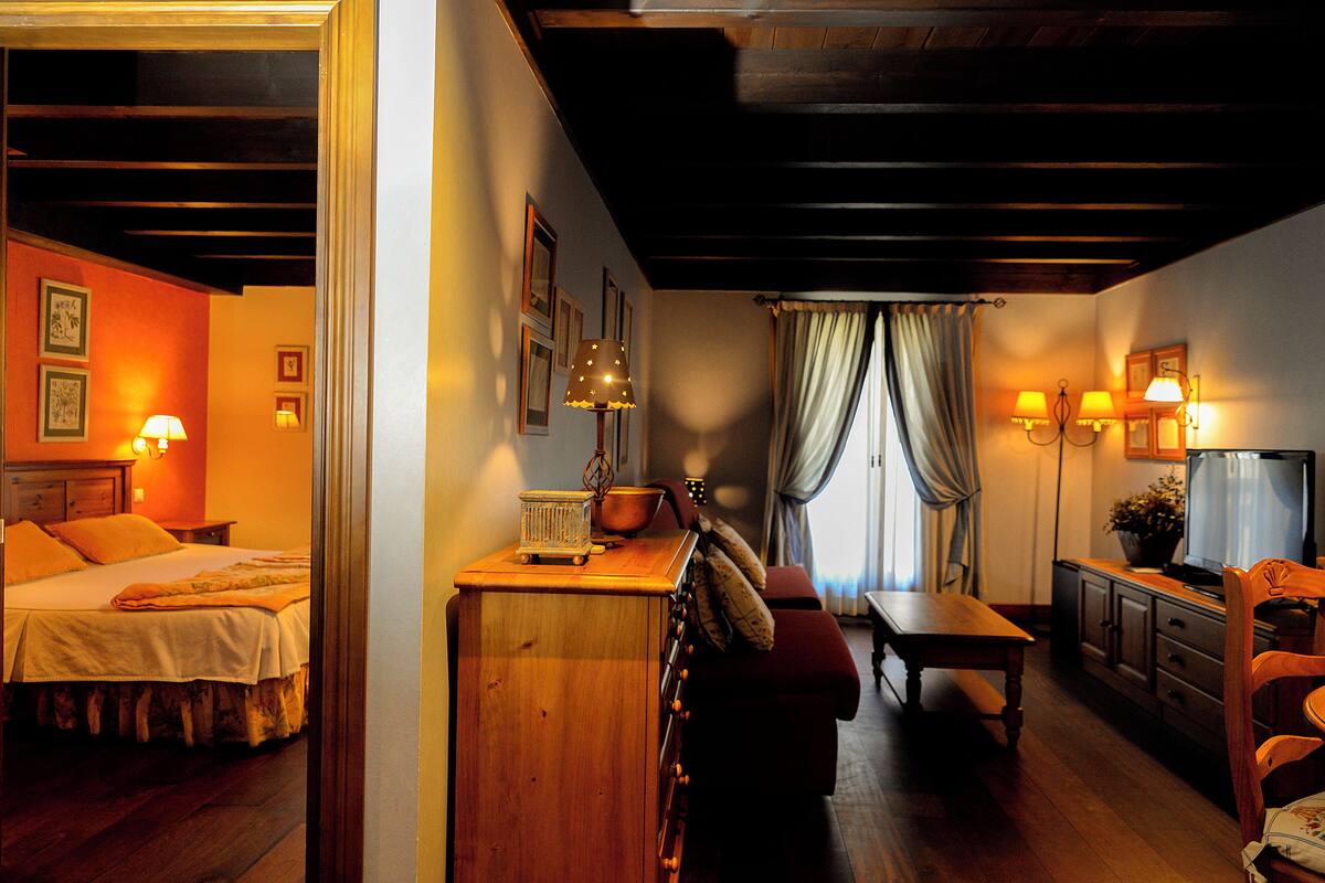 Una habitación acogedora con una cama, un aparador de madera, una mesa de comedor y un televisor.