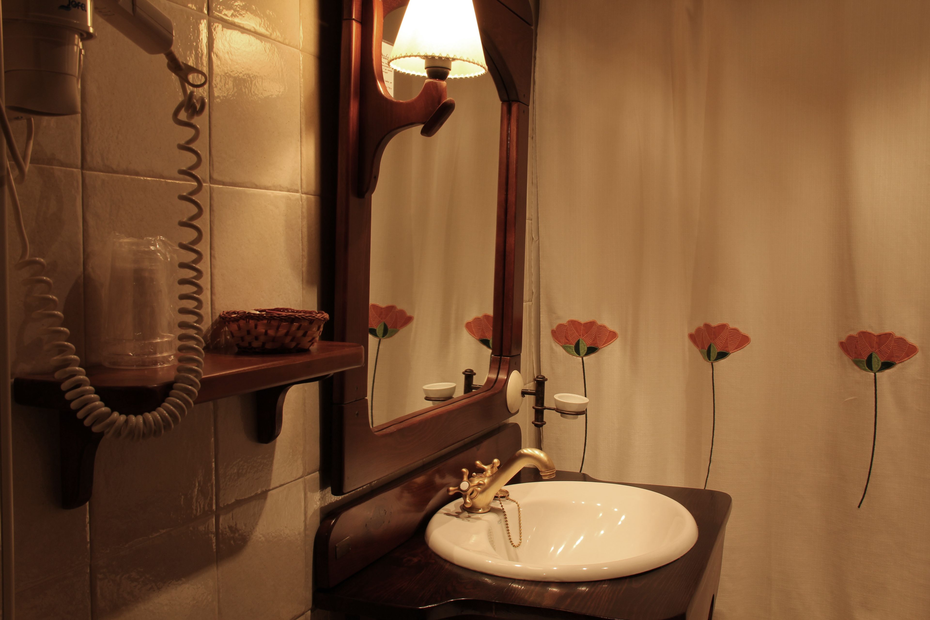 Un baño con un lavabo blanco, un mueble de tocador de madera, un espejo, un teléfono y una pared decorada con motivos florales.