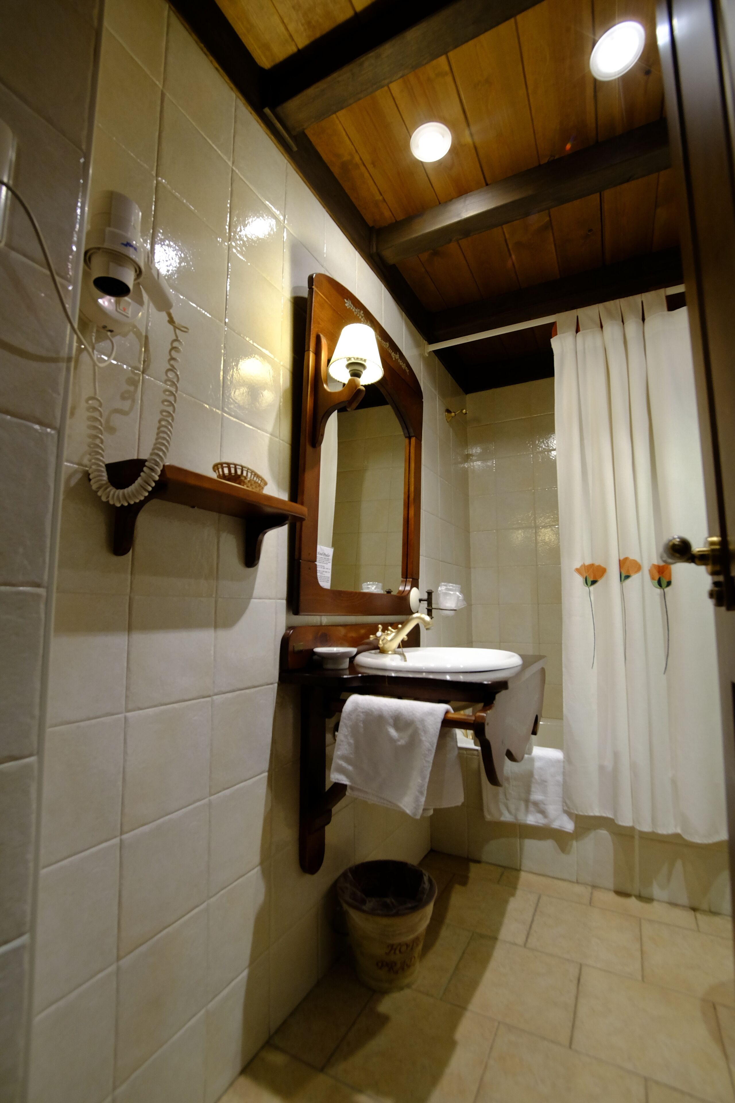 A bathroom with a wooden vanity, a mirror, a sink, a hairdryer, and a shower curtain.