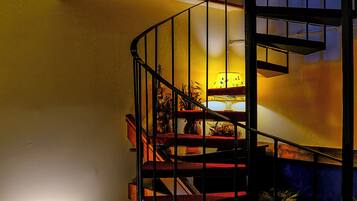 Eine Wendeltreppe mit rotem Teppich und schwarzen Geländern, die zu einem Podest mit einer Lampe und einer Pflanze führt.