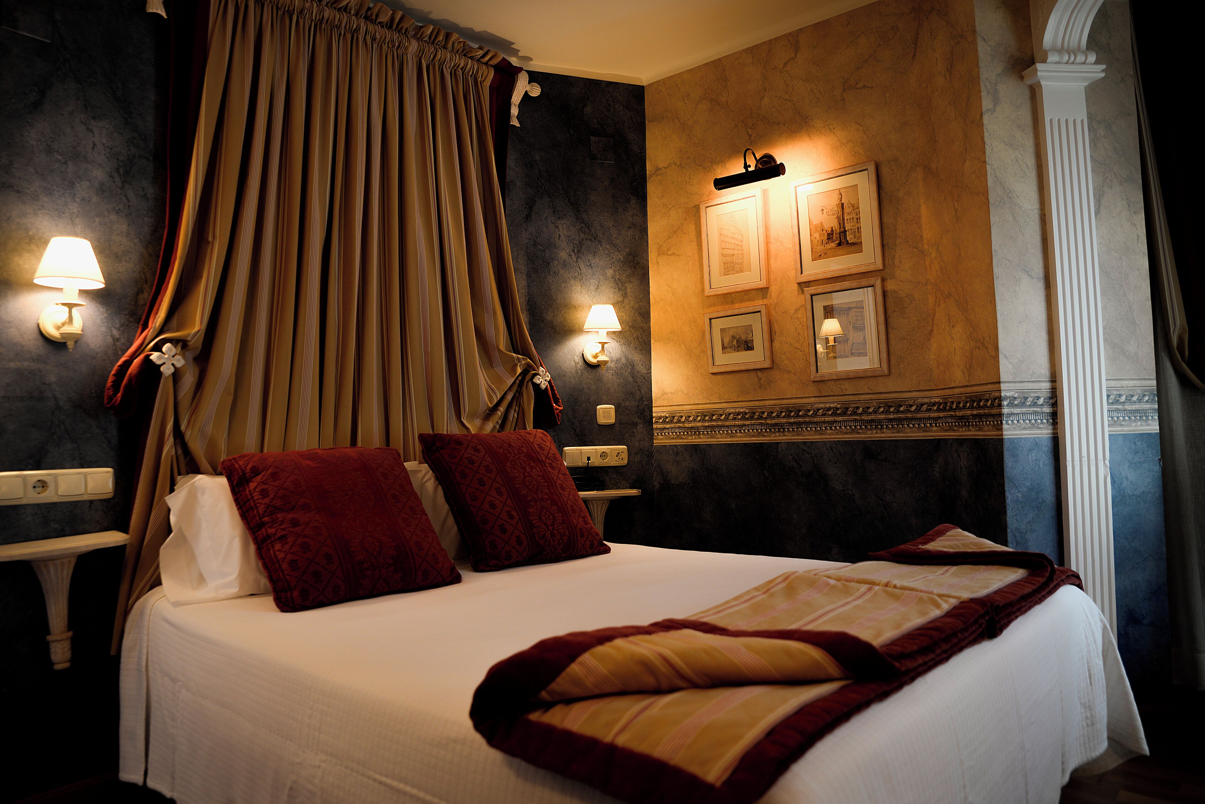 A hotel room with a large bed, two wall-mounted lamps, and a framed picture on the wall.
