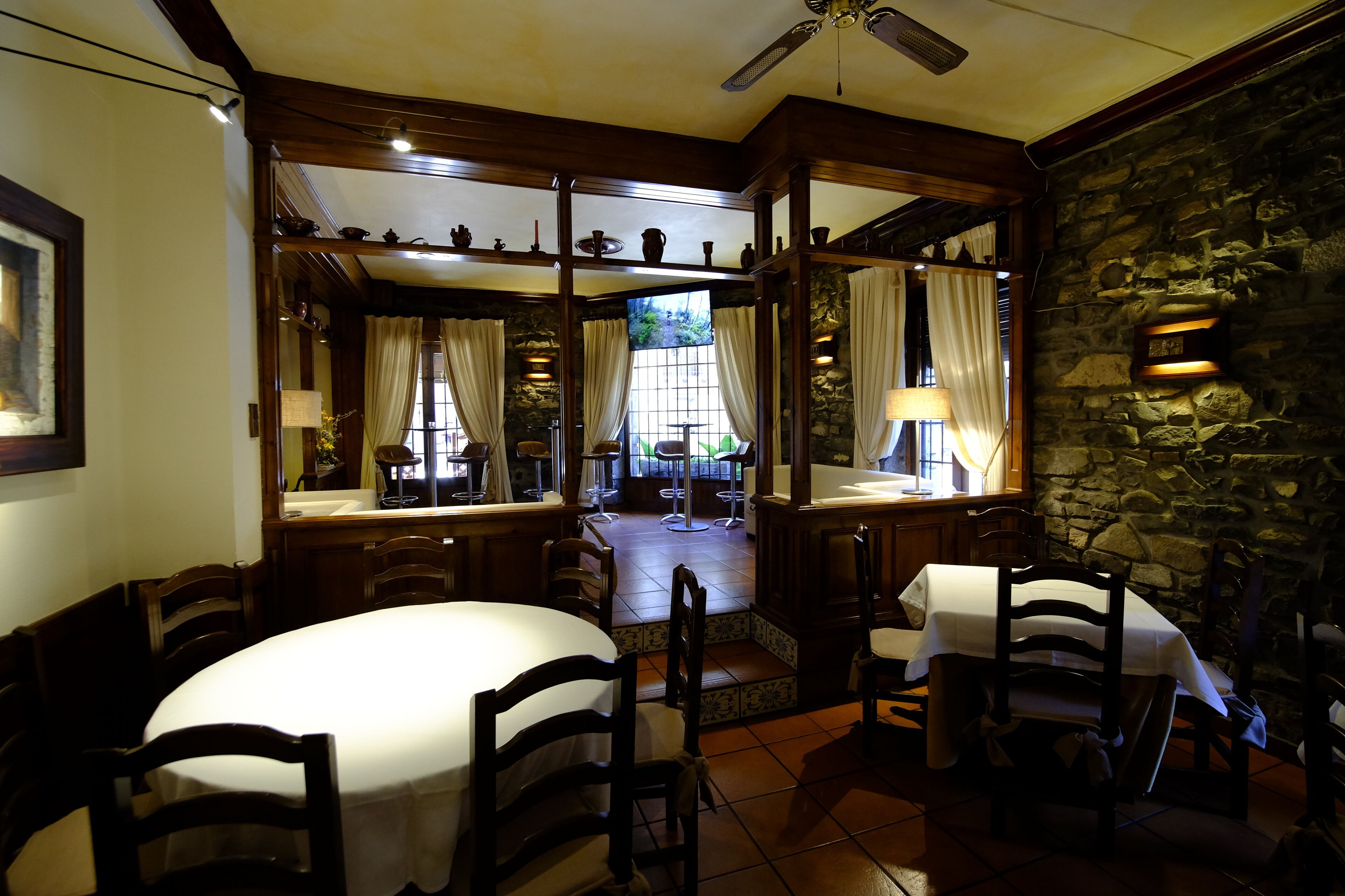 Comedor con pared de piedra, mobiliario de madera y vistas al exterior.