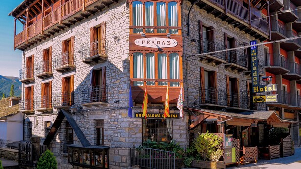 Un edificio de piedra tradicional con balcones de madera, un letrero que dice "Hotel Pradas" y banderas.