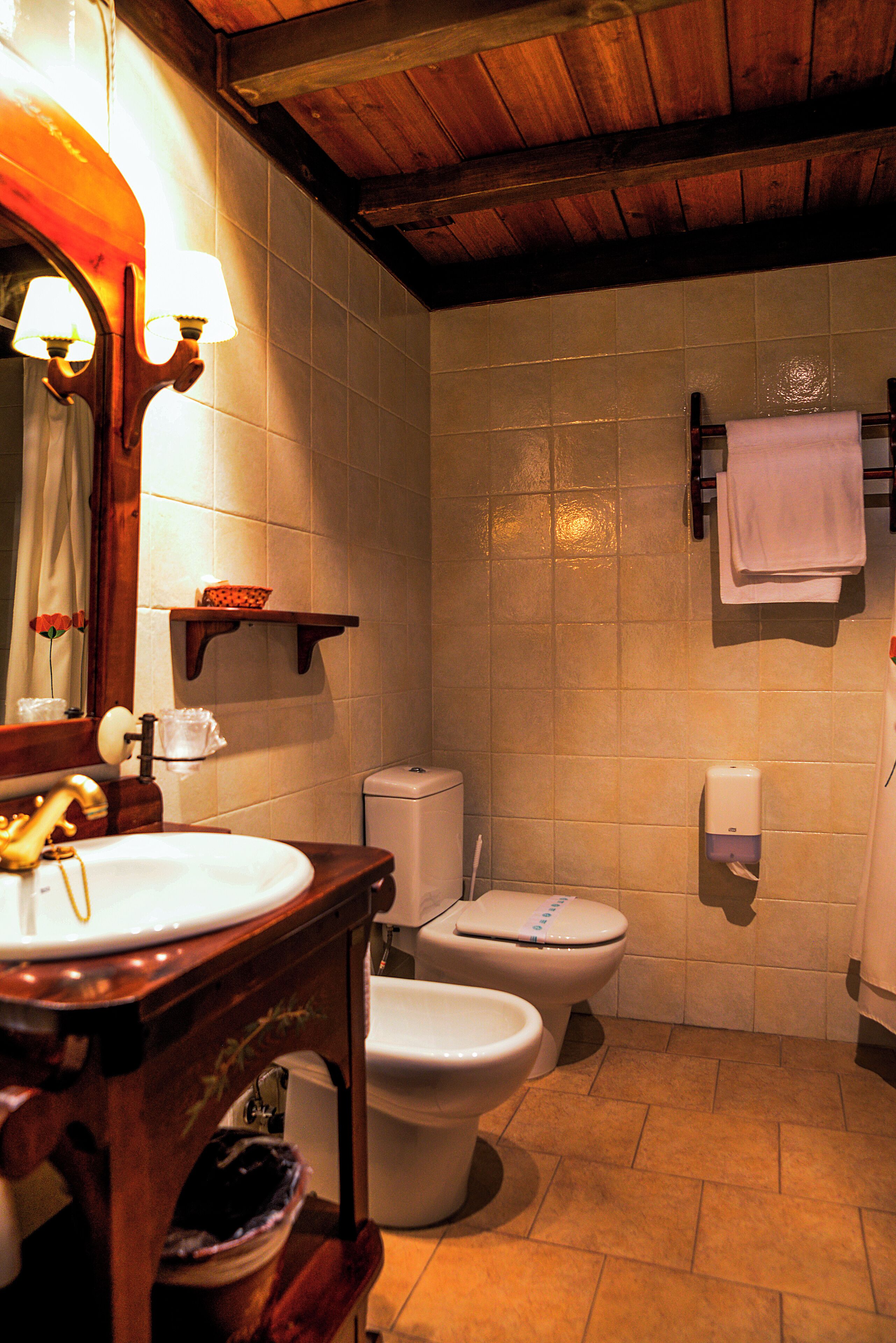 A bathroom with a wooden vanity, two toilets, a towel rack, and a soap dispenser.