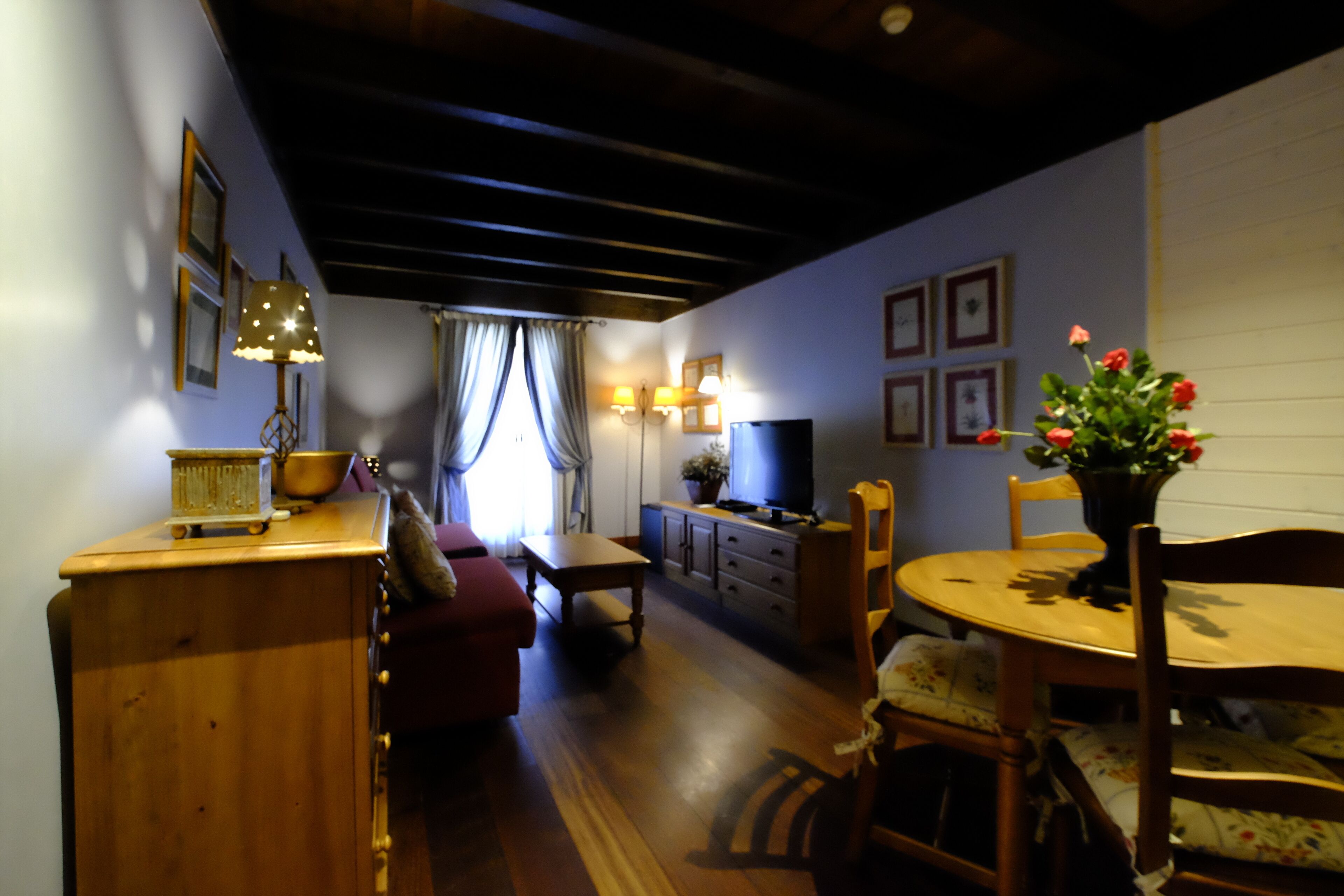 Una sala de estar acogedora con muebles de madera, televisor y un comedor con mesa y sillas.