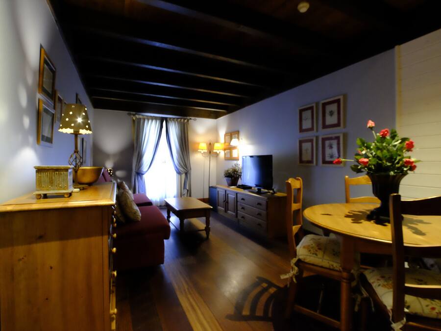 Ein gemütliches Wohnzimmer mit Holzmöbeln, einem Fernseher und einer Essecke mit Tisch und Stühlen.