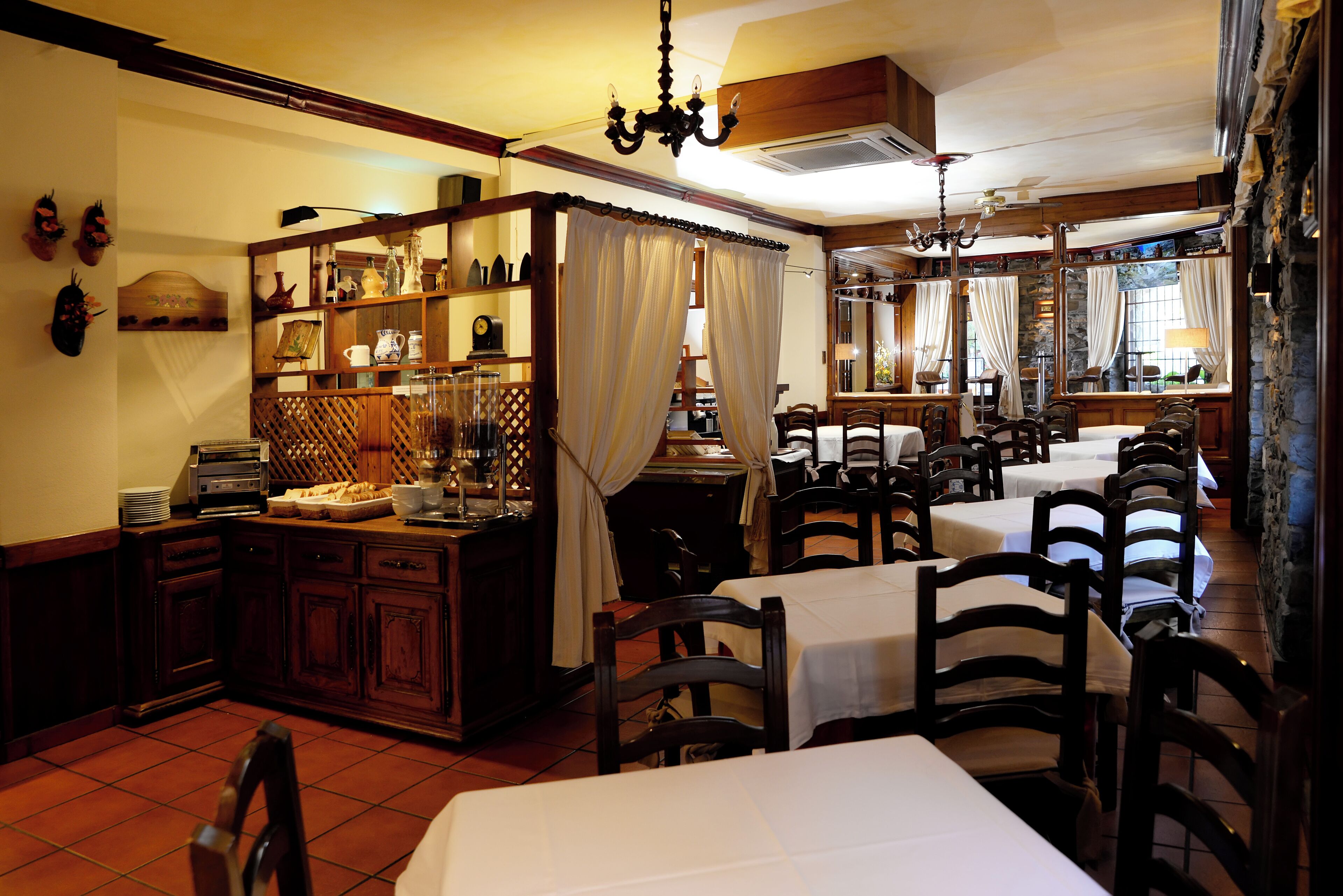 A traditional dining area with wooden furniture, white tablecloths, and a central buffet.