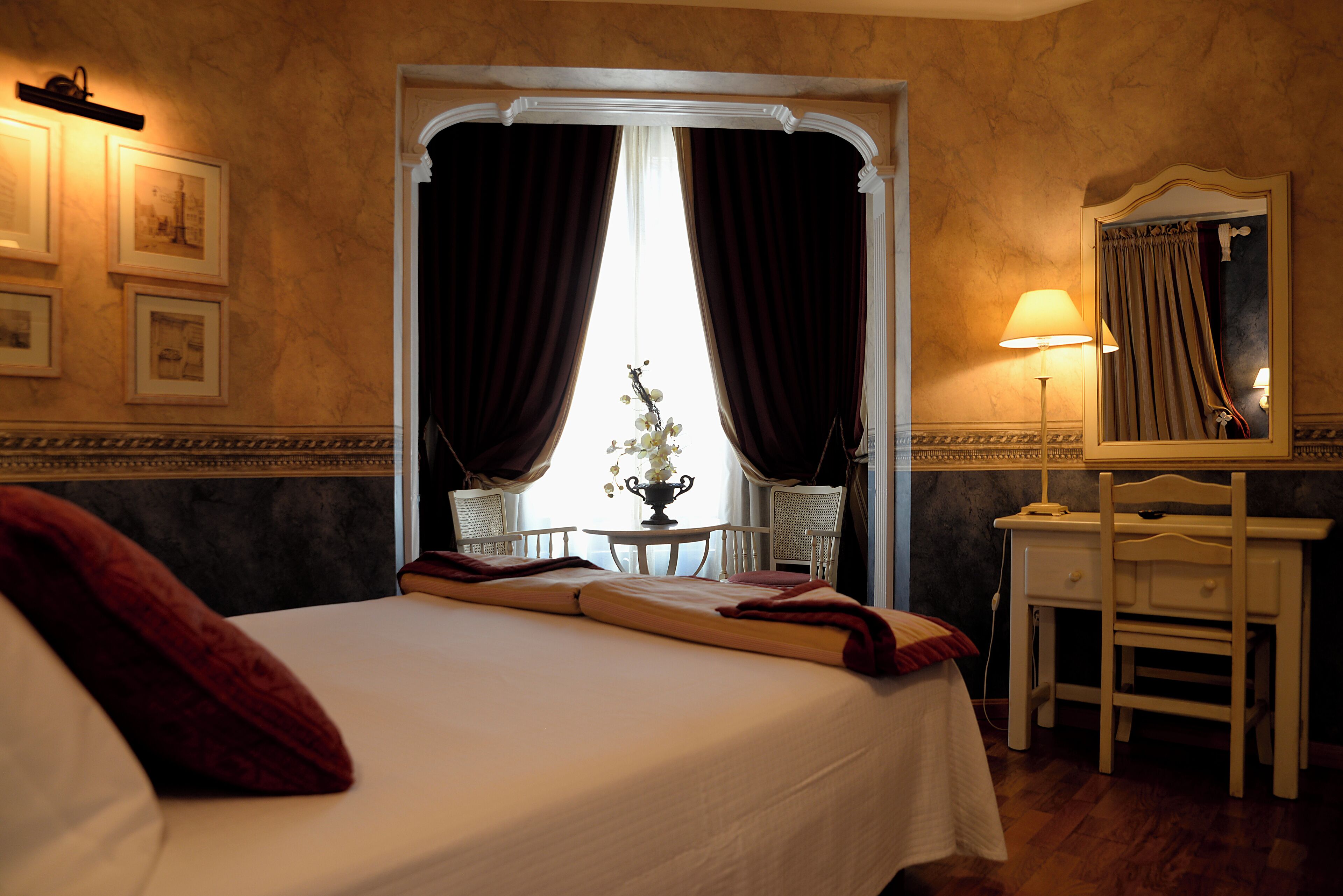 A hotel room with a bed, a desk, a chair, a lamp, and a mirror.